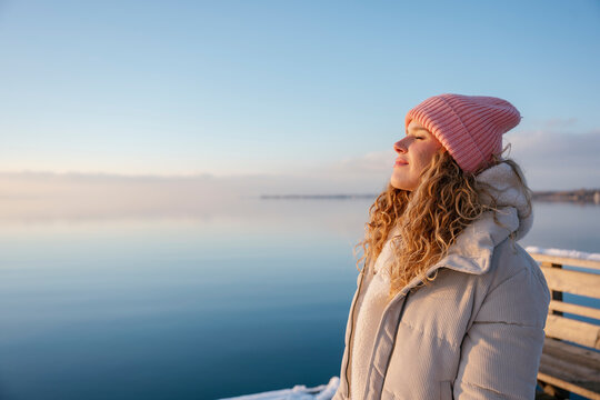 Woman standing by lake enjoying winter sunshine and practicing self-care