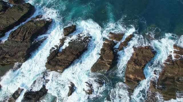 Aerial drone footage from above of Karang Taraje rock formation, in Legon Pari beach, Lebak Regency, Banten, Java island, Indonesia, with clear blue sea, and waves crushing, creating waterfalls over