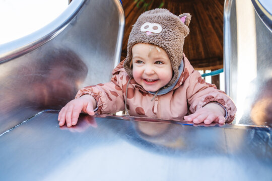 Smiling child in animal hat playing on slide outdoors in winter