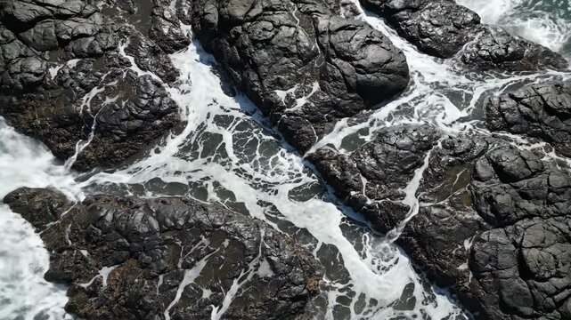 Ocean waves crash against rocky shoreline, creating foam and splashes, showcasing the dynamic interaction between water and stones in a coastal environment
