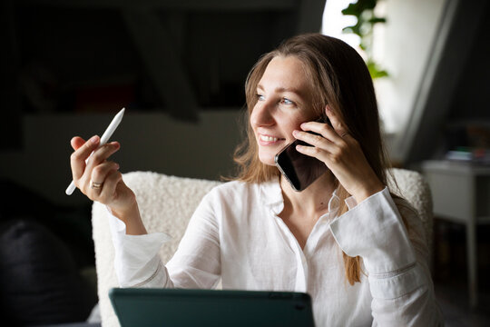 Smiling interior designer holding digitized pen talking on smart phone