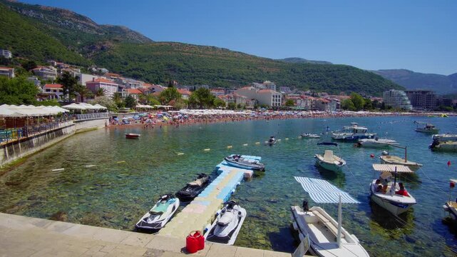 view of Petrovac harbor in Montenegro, a stone pier with boats, and the calm turquoise Adriatic Sea. A perfect summer travel and vacation scene