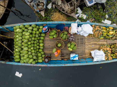 Aerial view of people trading with watermelons and pineapples on a boat in a waterway filled with water hyacinth, Dhaka, Dhaka Division, Bangladesh.