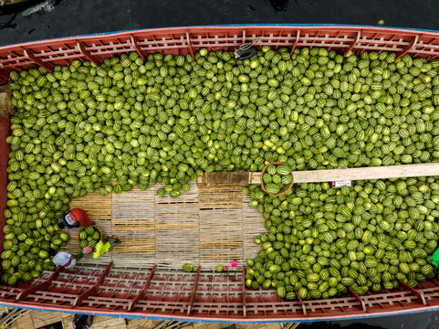 Aerial view of a boat brimming with vibrant green produce alongside workers, creating a striking contrast against the dark water, Dhaka, Dhaka Division, Bangladesh.