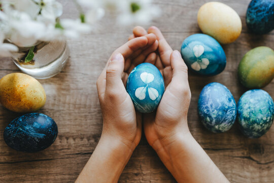 Hands holding blue Easter egg with flower pattern on wooden table