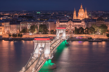Fototapeta premium Night view of the Szechenyi Chain Bridge illuminated in Hungarian flag colors and St. Stephen's Basilica in Budapest.