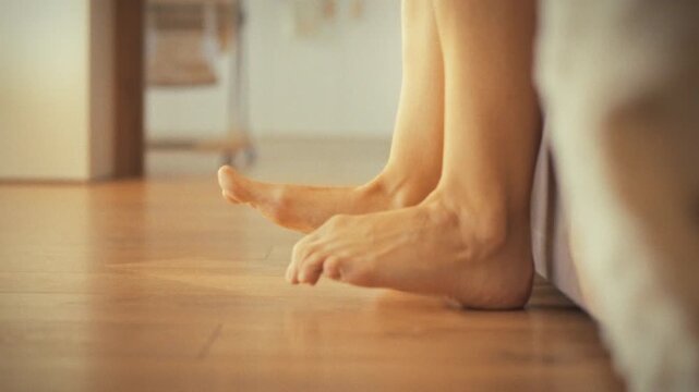 Young girl slowly lowers her bare feet from bed, stretching them after refreshing morning nap at home. serene start, she gently touches floor, savoring natural awakening moment, feeling revitalized