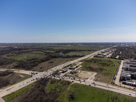 Aerial view of vehicles queuing at an intersection amidst a blend of urban development and natural landscapes, Frisco, Texas, United States.