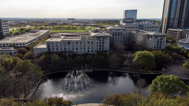 Aerial view of the dark lake reflecting the light sky, the fountain throwing water high up, and the buildings standing tall, Plano, Texas, United States.