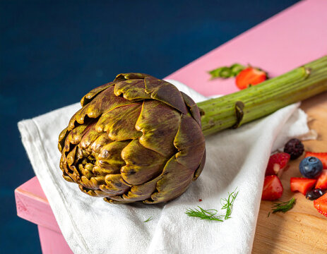An artichoke on a white cloth with mixed berries and fruits