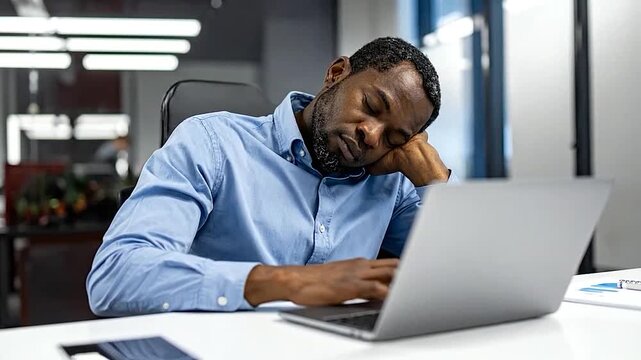 Exhausted man taking a nap while working on his laptop in a modern office