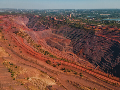 Aerial view of the vast, rust-colored Kryvyi Rih iron ore quarry scarred into the landscape, contrasting with the green city outskirts beyond, Kryvyi Rih, Dnipropetrovsk Oblast, Ukraine.