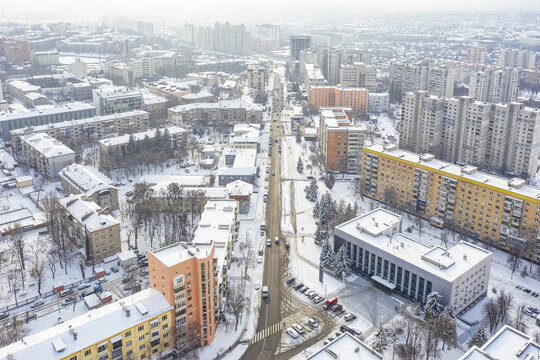 Aerial view of a snow-blanketed city street stretches towards the horizon, flanked by buildings painted in muted yellows and oranges, Kharkiv, Kharkiv Oblast, Ukraine.
