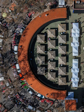 Aerial view of tents arranged in a semi-circle pattern with a red roofed structure, surrounded by cars and flea market in Cascais, Portugal