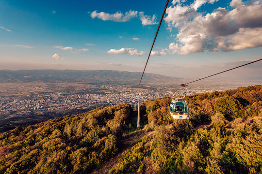 View of a cable car descends, offering a stunning panorama of the city nestled amidst rolling hills and a vast sky, Skopje, Greater Skopje, North Macedonia.