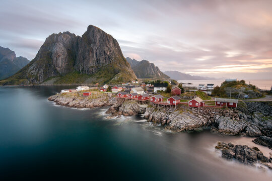 View of red cabins stand sentinel against the backdrop of towering mountains, where the sea whispers tales of time, Lofoten Islands, Nordland, Norway.