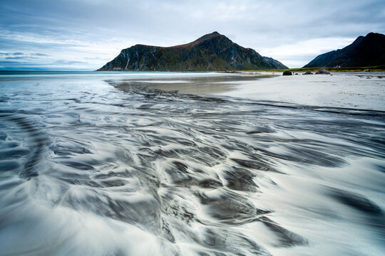 View of the dramatic patterns etched by the tide on the sandy beach beneath the watchful gaze of rugged mountains, a tranquil scene, Lofoten Islands, Nordland, Norway.
