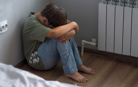 an offended child sits in the corner of the room. the boy hides his head in his knees, closing himself off from problems.
