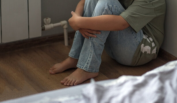 the legs of a child sitting alone in the corner of a room. The child wants to hide from the violence