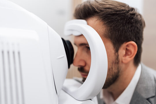 A professional male patient receives a vision checkup using a modern autorefractor at an optometry clinic while doing diagnostic health screening for optimal eyesight. Focus on device in foreground.