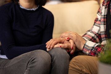 Caucasian husband and wife sit closely on couch, holding hands during counseling to express unity and emotional support. Close up shows couple supportive handhold, reflecting trust and connection.