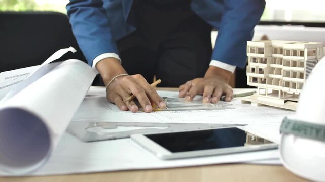 Close-up of architect's hands works on building layout design in the office desk. Designer at table drawing on blueprint or draft design of modern building manufacture.