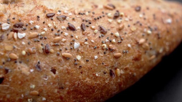 Baked bread crust covered with mixed seeds including flax sesame and poppy. Rustic artisan bakery product on black background