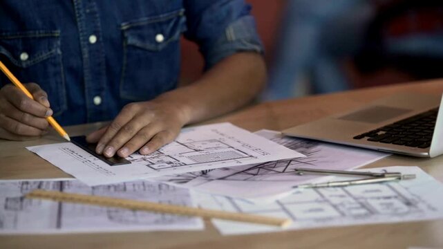 Architect designer drawing close-up. Professional architect working, making notes in new house project, blueprint plan, drafting building. Architect using Ruler and Pencil to make Blueprints on Paper.