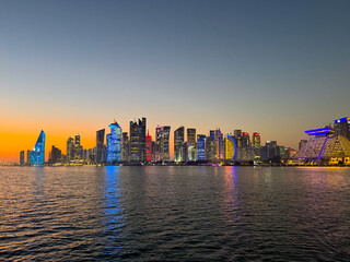 Obraz premium Doha West Bay skyline at sunset with illuminated skyscrapers and reflections on the Persian Gulf. Modern skyline of Doha West Bay at sunset with colorful illuminated skyscrapers reflecting.