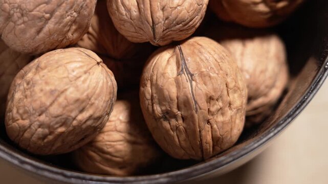 Organic dried walnuts in ceramic bowl on brown background close up. Rotation