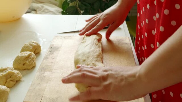 Close-up of hands shaping, cutting and portioning dough on a floured wooden board for homemade baking