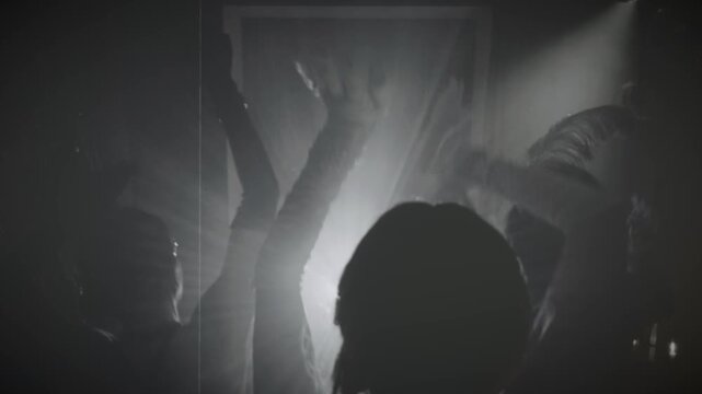 1920s old style sepia color film, people hang out dancing crowd hands arms raised up waving to sides in dark night club. Youth flapper female male have fun at dance floor roaring twenties retro party.