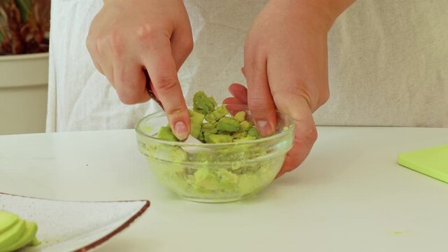 Avocado mash process, female hands preparing guacamole in kitchen