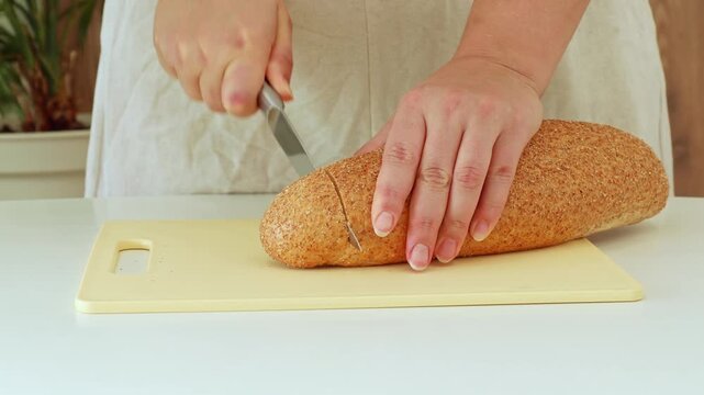 Closeup of hands slicing and cutting seeded bread on board during morning preparation scene