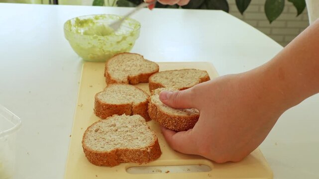 Female hands making sandwich with mashed avocado slices and wholegrain bread for breakfast