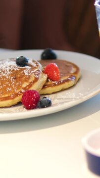 Traditional Eastern European oladyi pancakes presenting golden surface, accompanied by tangy sour cream, vibrant berry sauce, and fresh seasonal berries beside orange juice