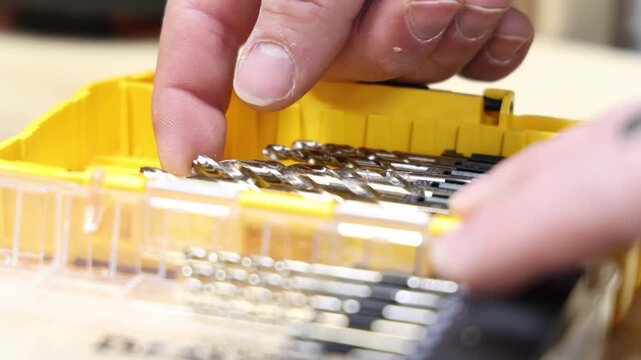 Close-up of a hand selecting a drill bit from a yellow storage case