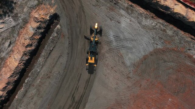 Aerial view of a Caterpillar motor grader on a dirt road on a sunny day. The camera tilted down dolly in over the road following the machine in motion