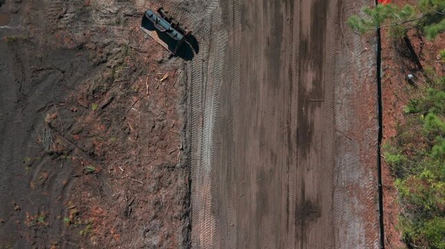 Aerial view of a Caterpillar motor grader, a construction vehicle on a dirt road, shot on a sunny day. The camera tilted down dolly in over the road following the machine passing a parked dump truck.