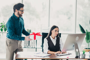Gift exchange at a modern office as colleagues present a wrapped gift to a businesswoman at a...