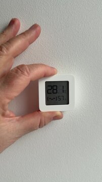 Hand mounts digital sensor on textured wall showing and humidity closeup of woman's hand placing compact white device homeowner.
