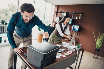 Two colleagues in a bright modern office celebrate success by a printer and desk covered with notes...