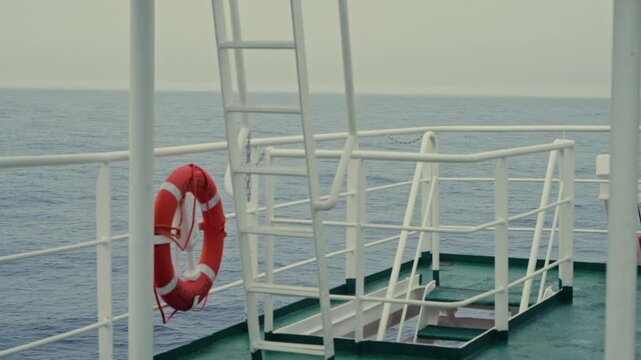 Quiet empty green expedition ship deck with red lifebuoy white metal railings and ladder overlooking calm grey polar ocean under overcast Antarctic sky