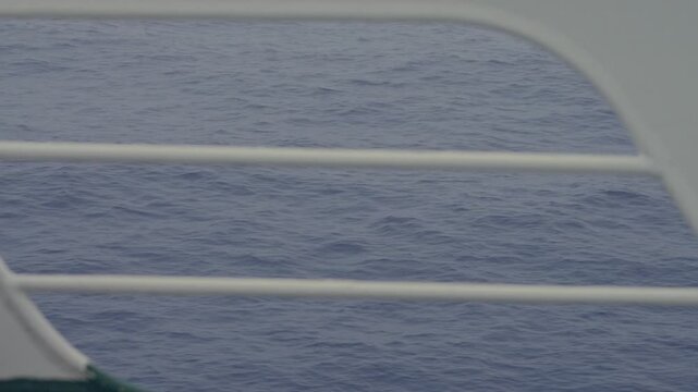 Fast moving choppy ocean waves viewed through white ship deck railing from aboard vessel sailing open sea