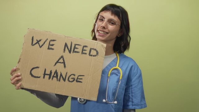 Woman nurse wearing blue scrubs holds cardboard sign reading we need a change in studio; hope activism reform.