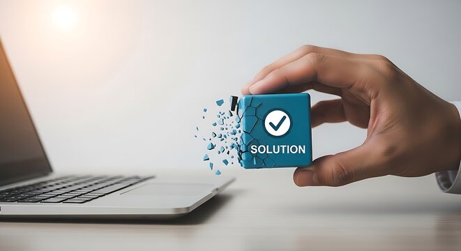 A hand holds a blue solution box with a checkmark emerging from a laptop on a desk in an office.