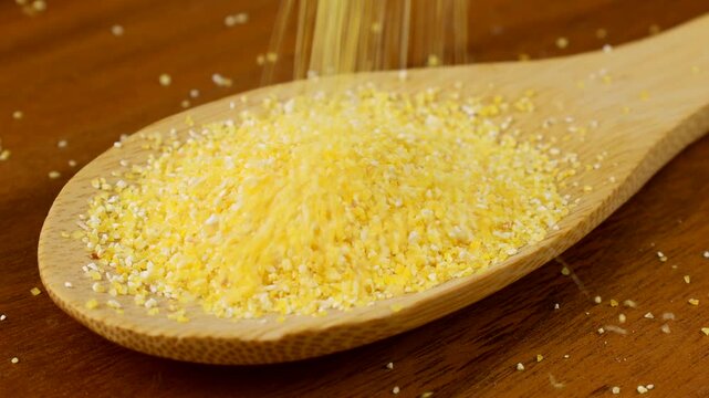 Yellow corn grain flour for polenta porridge falling down into the wooden spoon close up