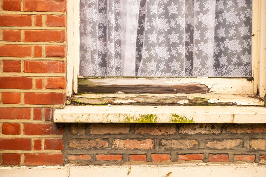 Rotten peeling wooden window frame on red brick house exterior