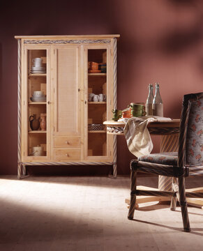 Still life of a wooden display cabinet and table with rattan chair