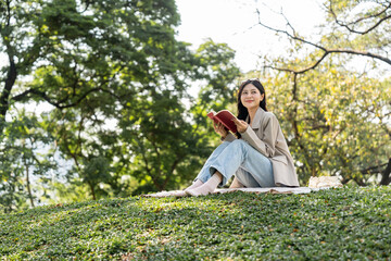 Young asian woman relaxing reading book sitting at public park life style outdoor. Happy female Take a break enjoy time living in the nature. Human and nature together